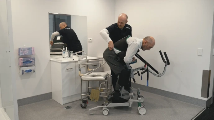 Single caregiver transferring an elderly man in the bathroom using the Kera sit2sit hoist